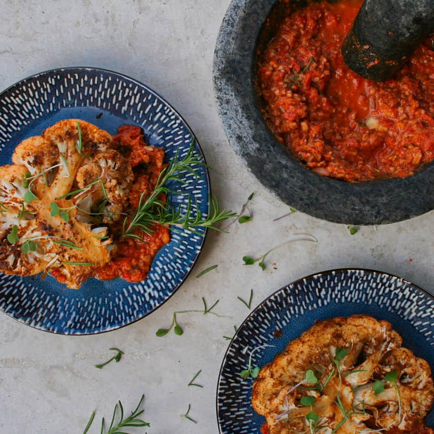 cauliflower steaks with a bowl of freshly crushed romesco in a mortar and pestle